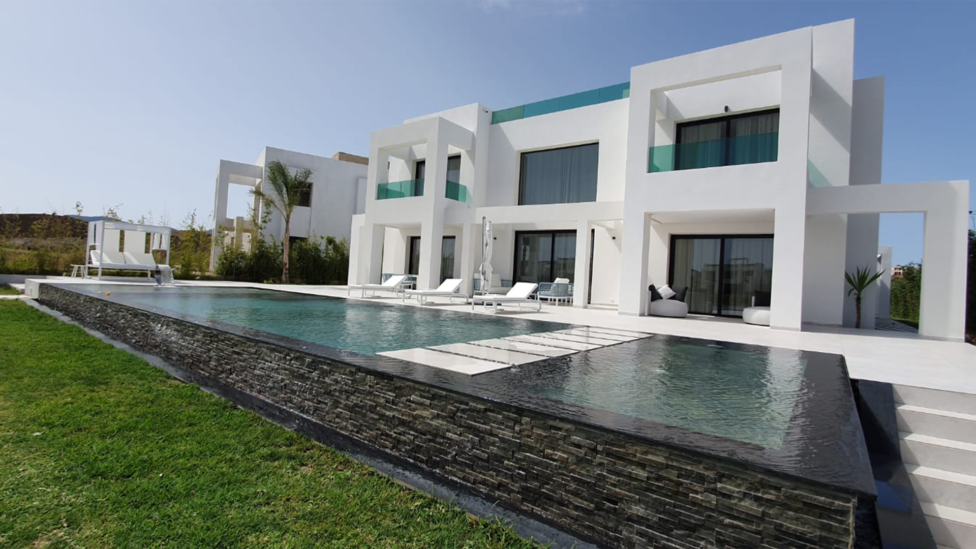 Villa blanche et piscine à débordement dans leur environnement paysager