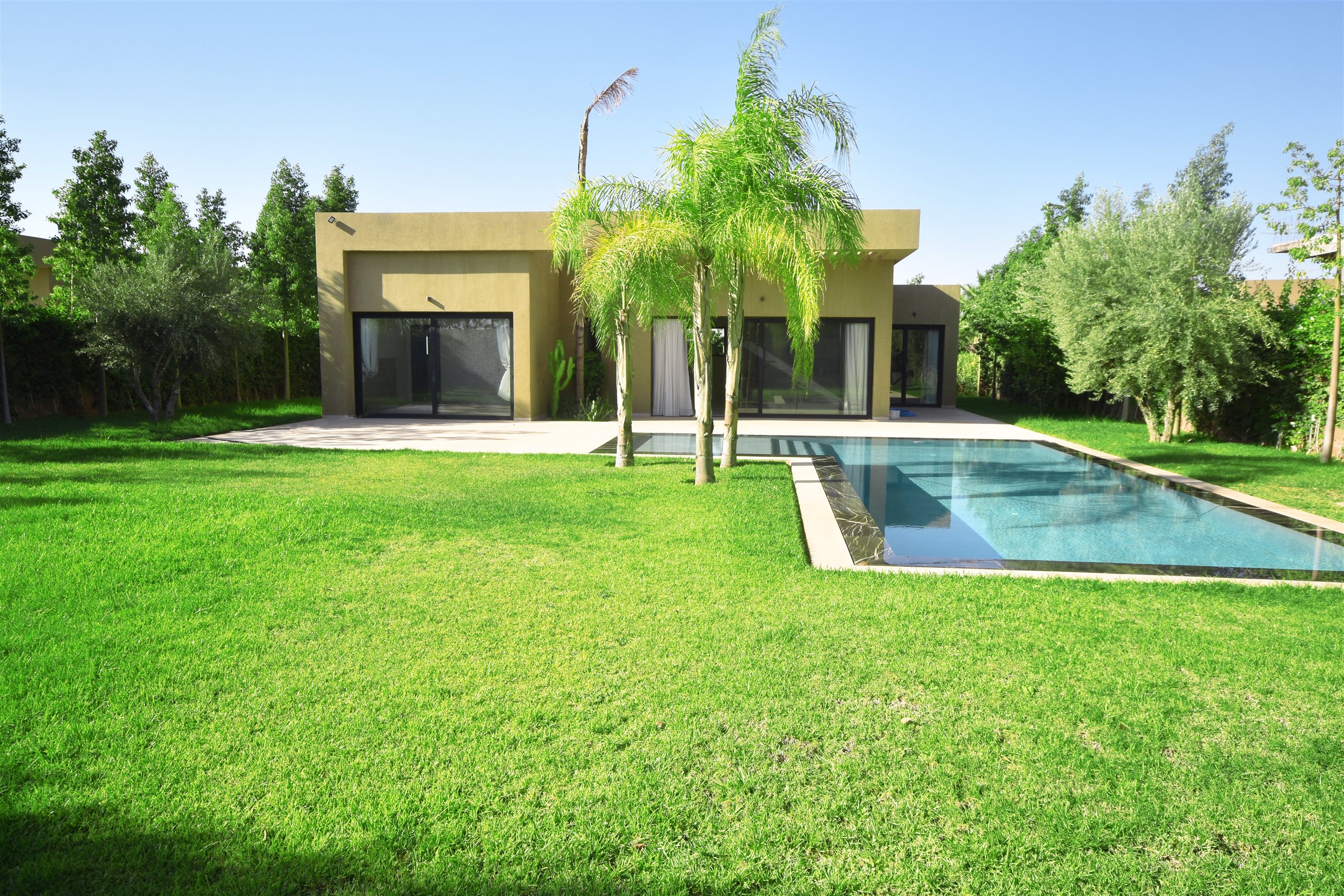 Façade vitrée de la villa ouverte sur la piscine et le vaste jardin arboré